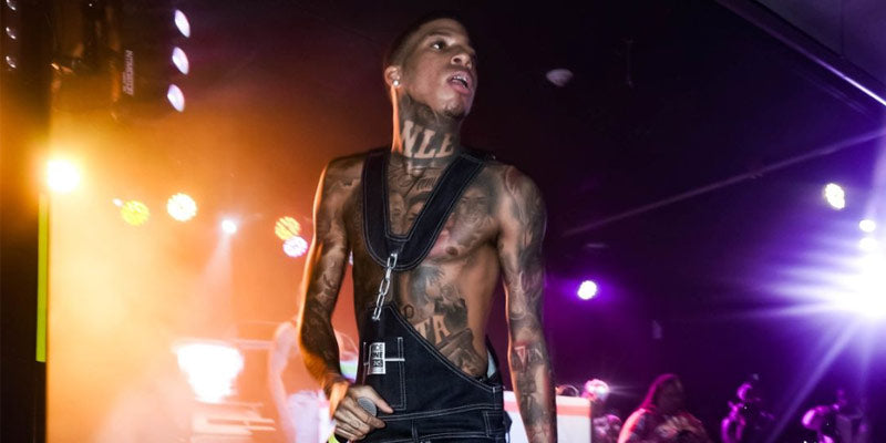 NLE Choppa captivates a Philadelphia audience, sporting Maurice Malone's 2024 preview of iconic 90s fashion denim overalls with a tattoo-laden, shirtless torso. The garment's standout chain link accents and baggy fit solidify its status as one of the best overalls ever. Photo credit: @kpfilmedit.