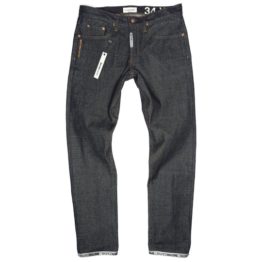 A pair of Maurice Malone jeans in raw 15 oz. Japanese selvedge denim, featuring a woven logo cuff, branded fly labeling, copper rivets, and orange stitching. The jeans are displayed flat, showcasing their handcrafted details and modern slim fit.