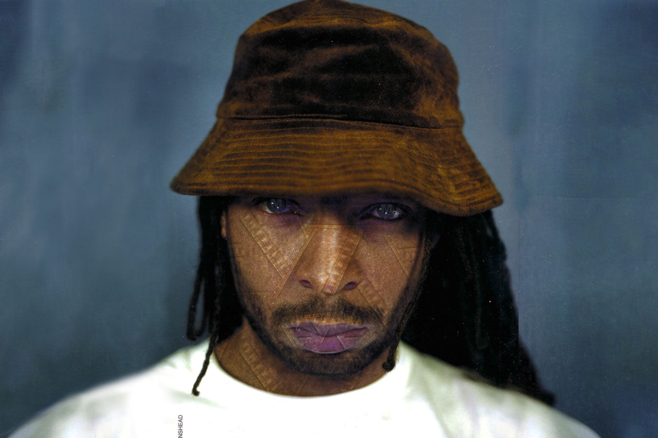 A close-up image without text, designer Maurice Malone, with subtle denim stitching visible in his skin and piercing eyes that mirror jean buttons, appears in his famed late 90s print advertisement. A true artist, Malone conceives, photographs, models, and produces the artwork in many of his ad campaigns under his alias Lenshead.